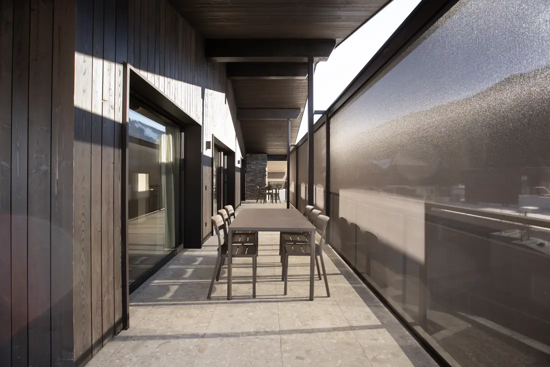 Überdachte Terrasse mit Tisch und Stühlen vor der Glasfront